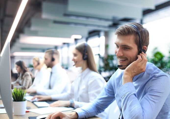 Portrait of call center worker accompanied by his team. Smiling customer support operator at work. SaaS Sales Recruiters hiring a team at a call center CCaaS.