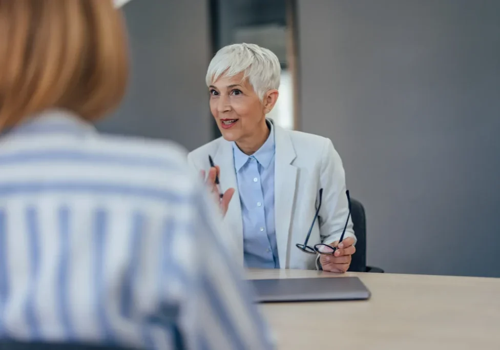 A confident sales candidate leading an interview conversation across a conference table, gesturing while the hiring manager listens.