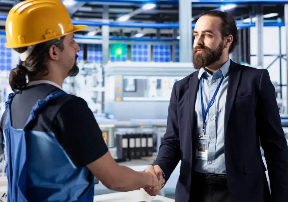 Manufacturing sales manager shaking hands with production floor worker inside an industrial factory