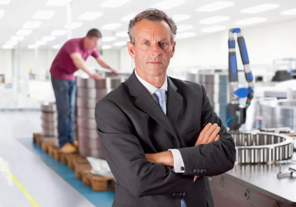 manufacturing sales executive standing in industrial factory with engineering equipment and production team in background